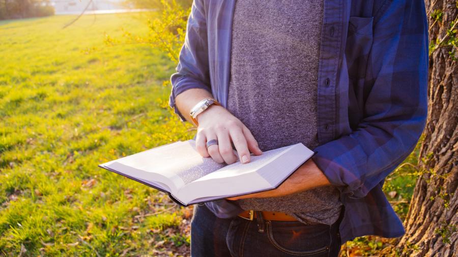 En mand der holder en åben bog foran en græsplæne