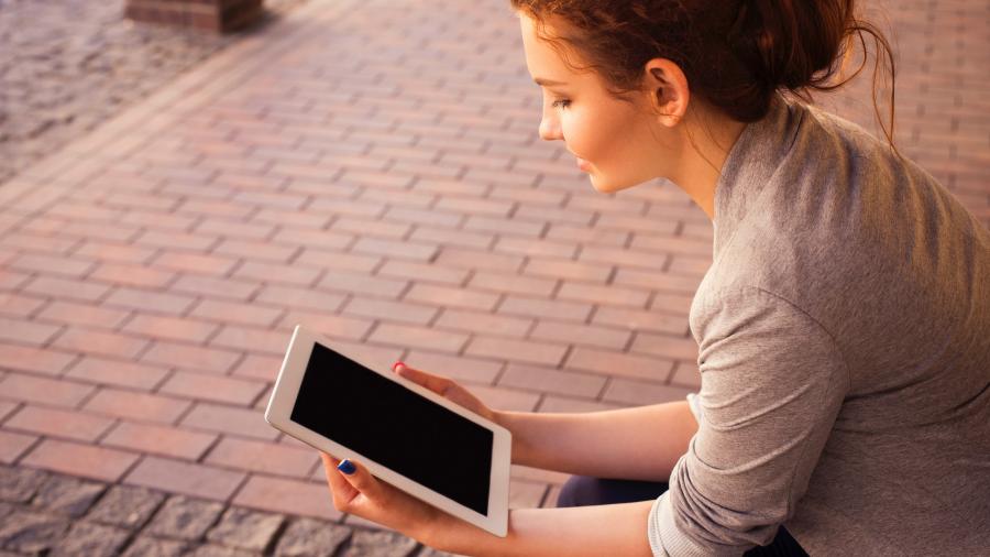 Kvinde på en bænk der læser på en elektronisk tablet.