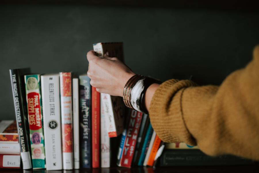 en arm iklædt brun sweater er ved at vælge en bog fra en hylde med bøger
