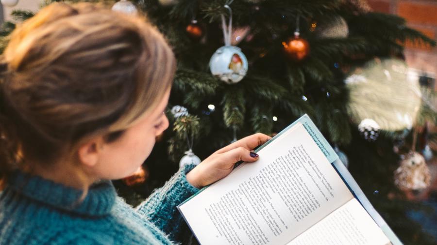 en kvinde der sidder foran et juletræ og læser i en bog