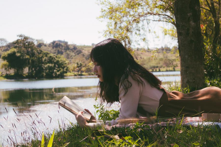 Kvinde ligger ved en skovsø og læser