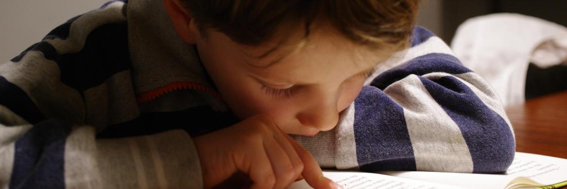nærbillede af dreng med næsen i en bog og fingeren presset mod papiret